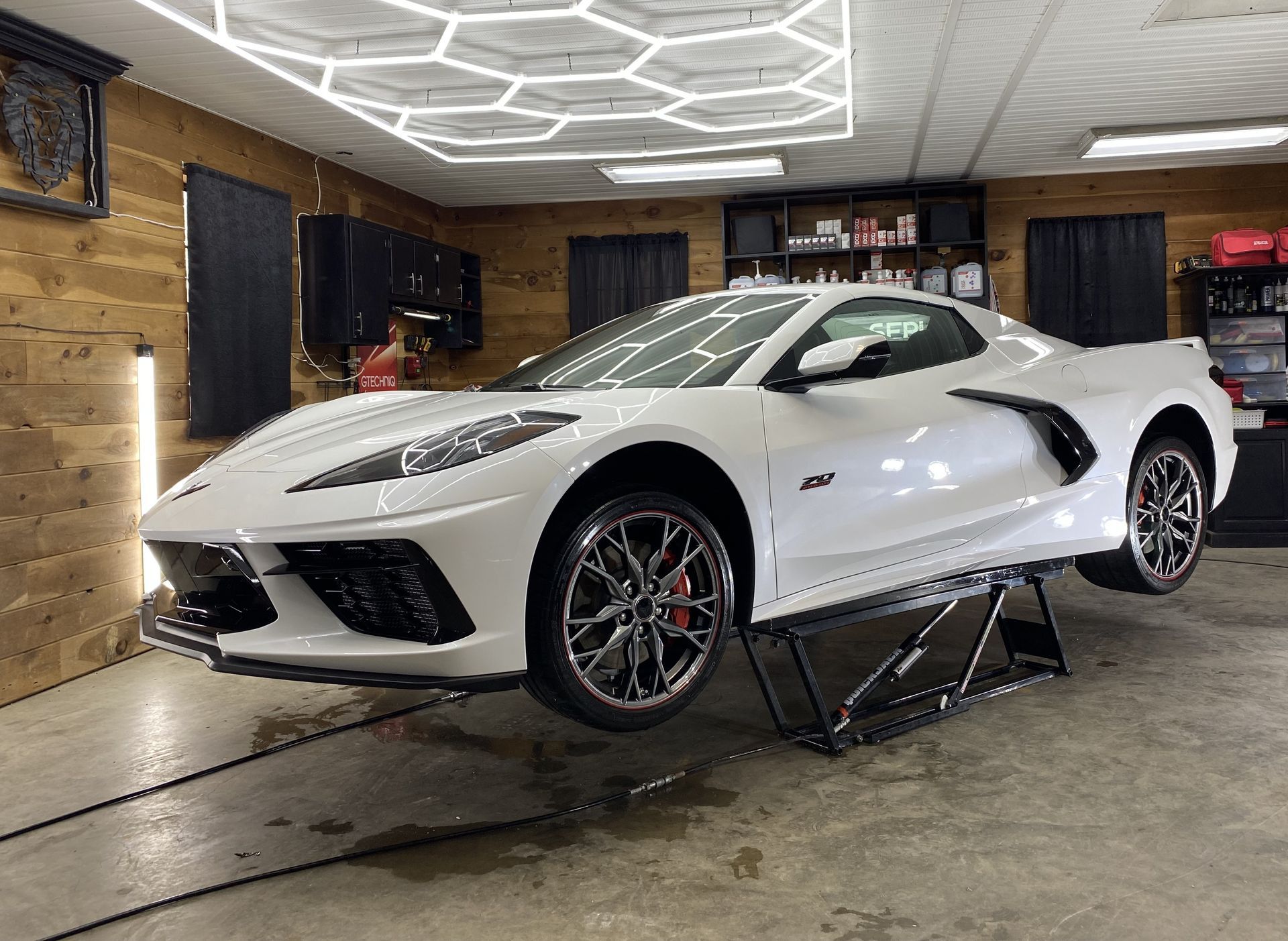 A white corvette is parked on a lift in a garage.
