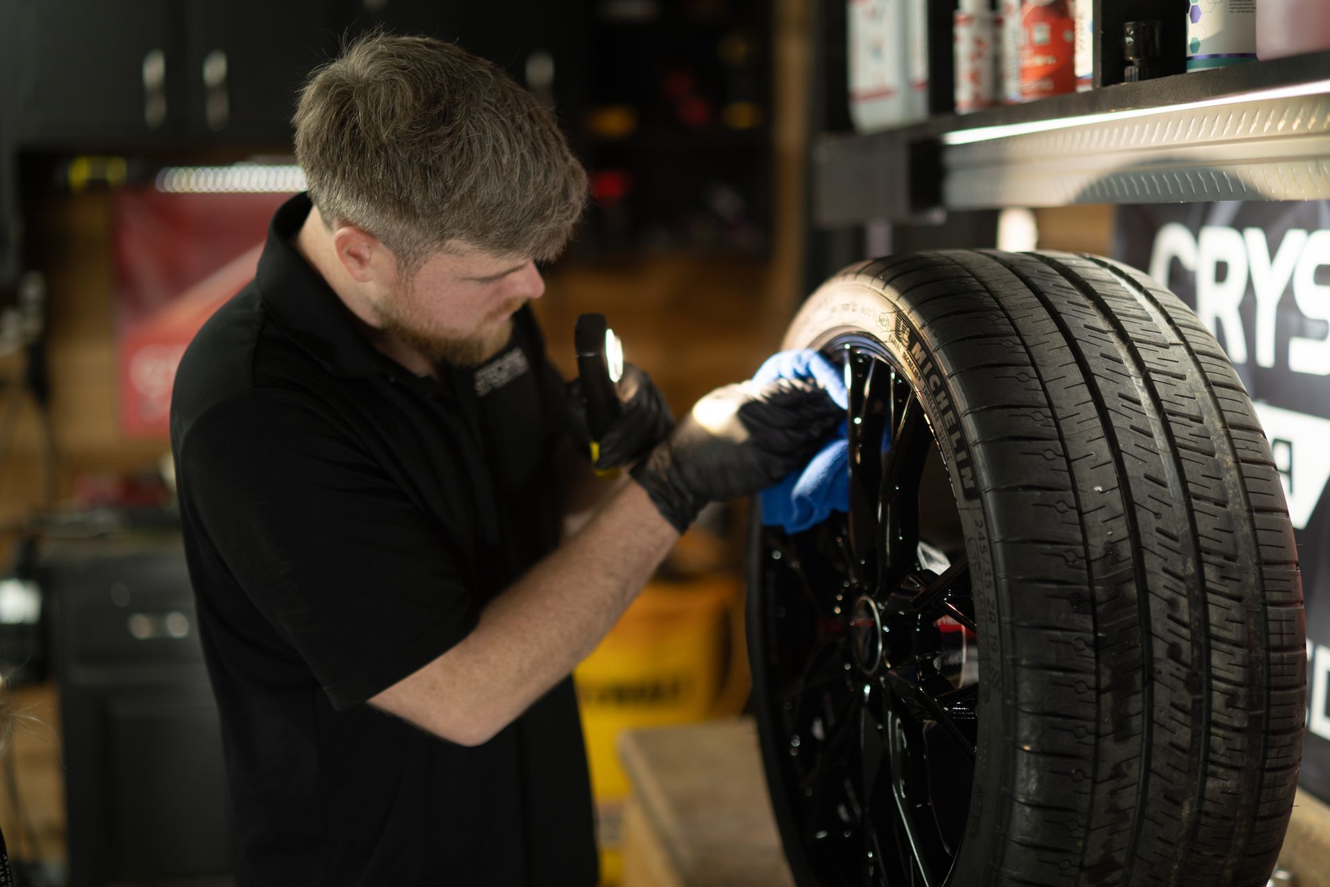 A man is cleaning a tire with a cloth in a garage.