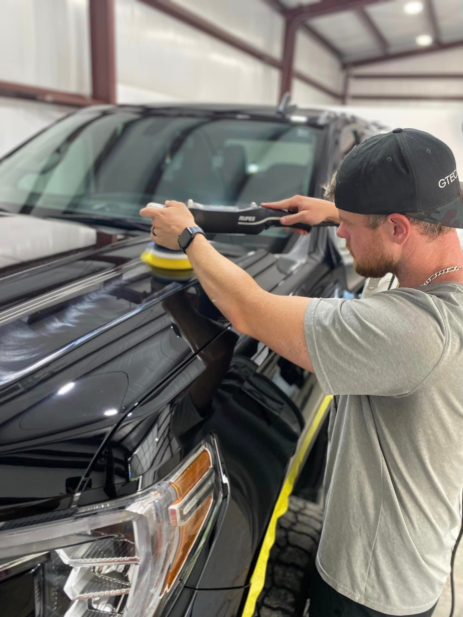 A man is polishing the hood of a black truck.