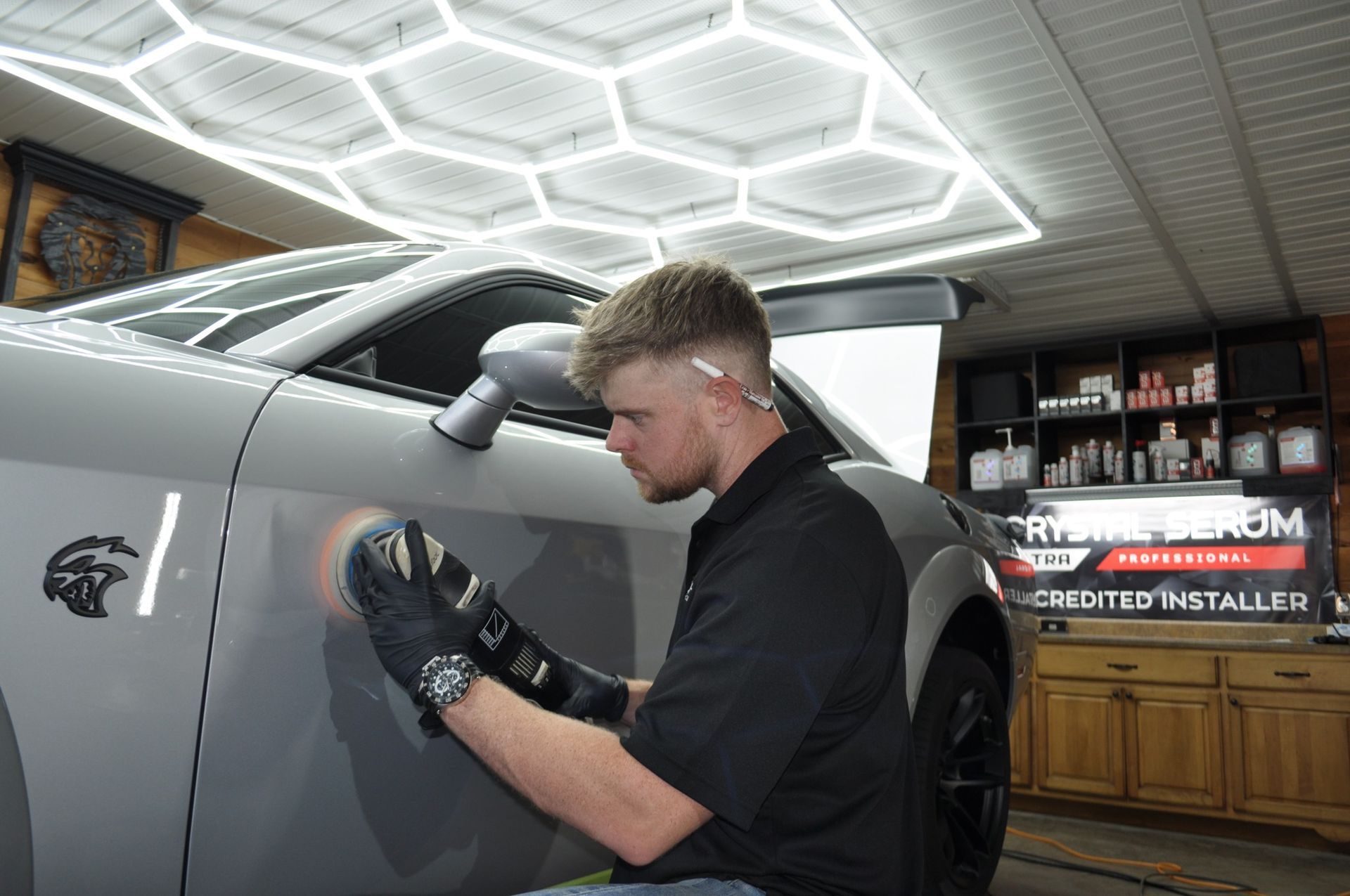 A man is polishing the side of a car in a garage.