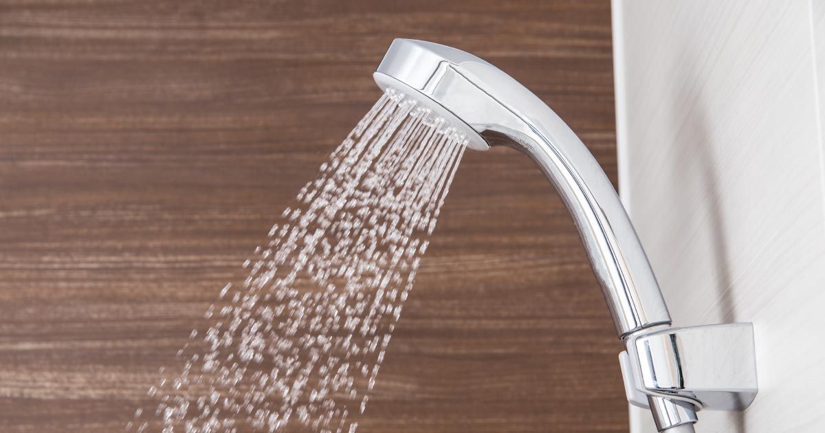 A shower head is spraying water on a wooden wall.