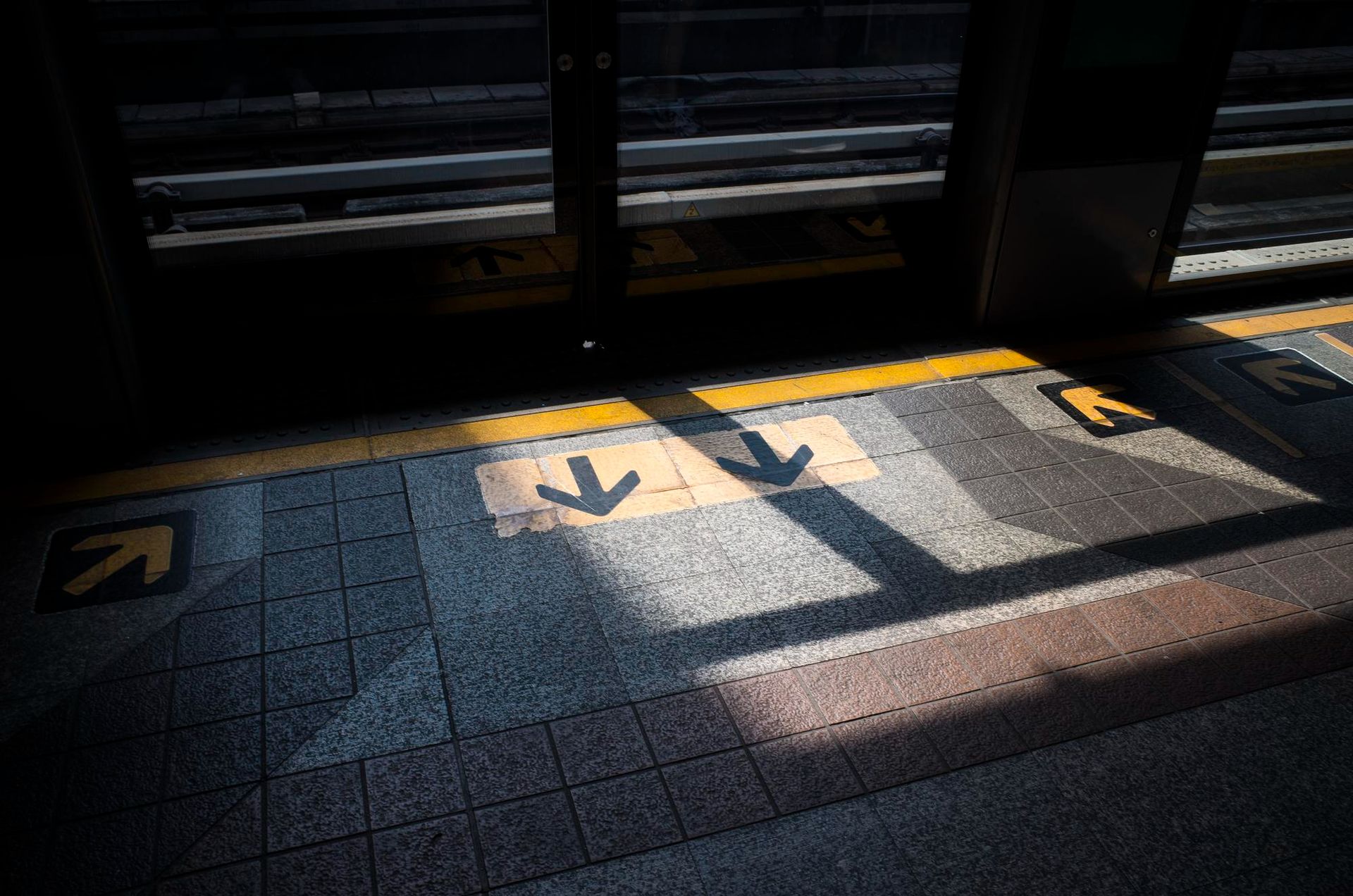 Platform edge with arrows, a yellow line, and sunlight shadows.