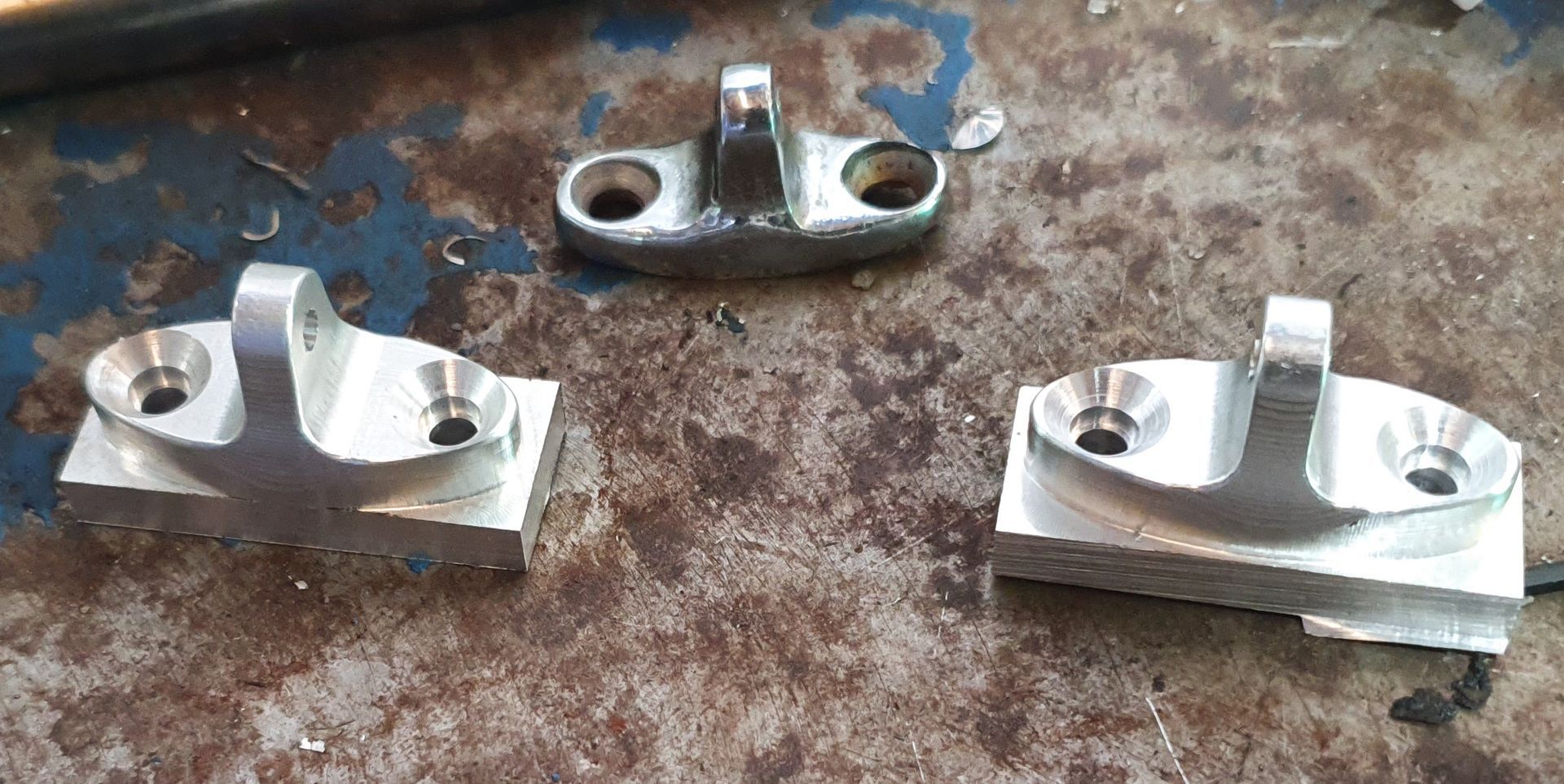 Three metal pieces are sitting on a rusty surface.