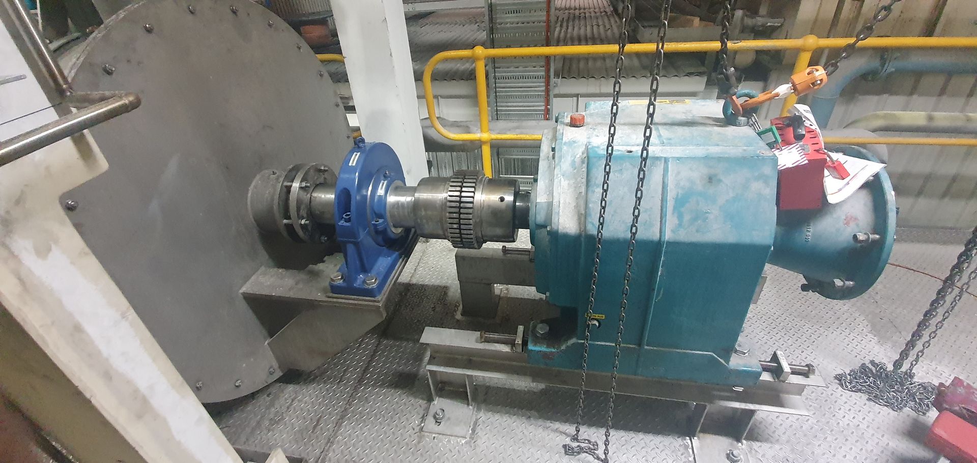 A large blue machine is being lifted by chains in a factory.