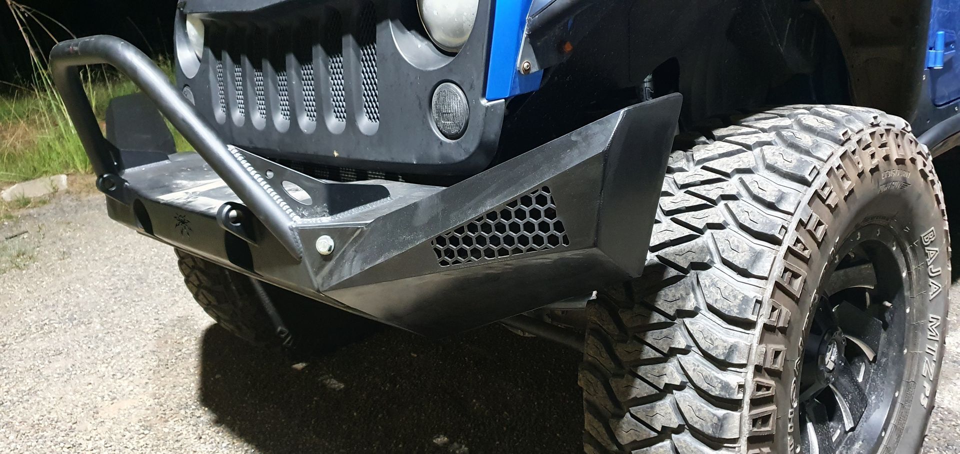 A blue jeep with a black bumper and black tires is parked on the side of the road.