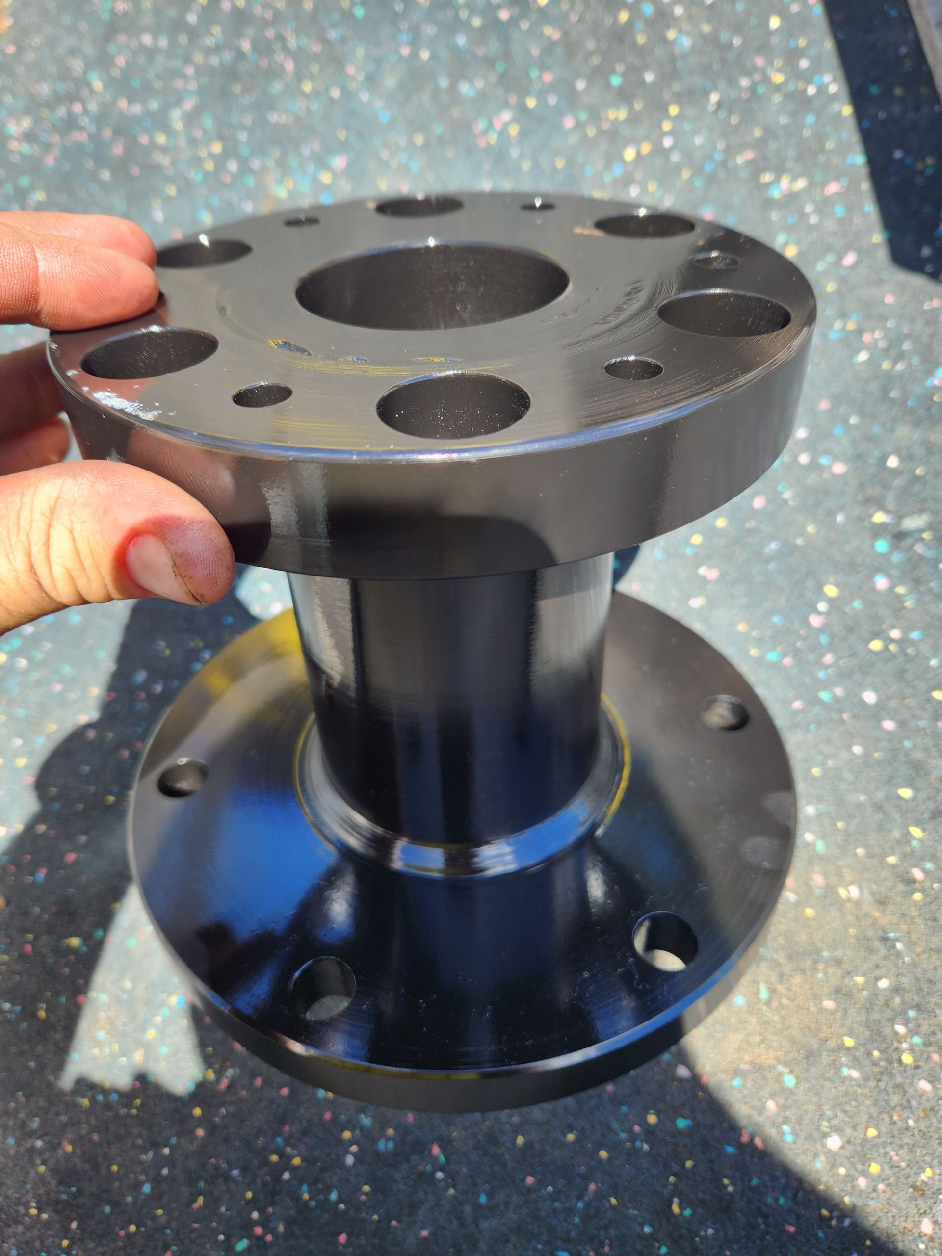 A person is holding a black metal flange on a table.