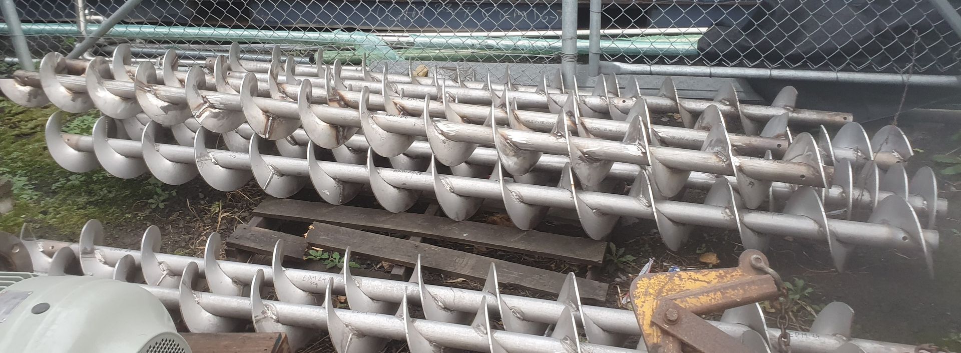 A bunch of metal pipes are stacked on top of each other in front of a chain link fence.