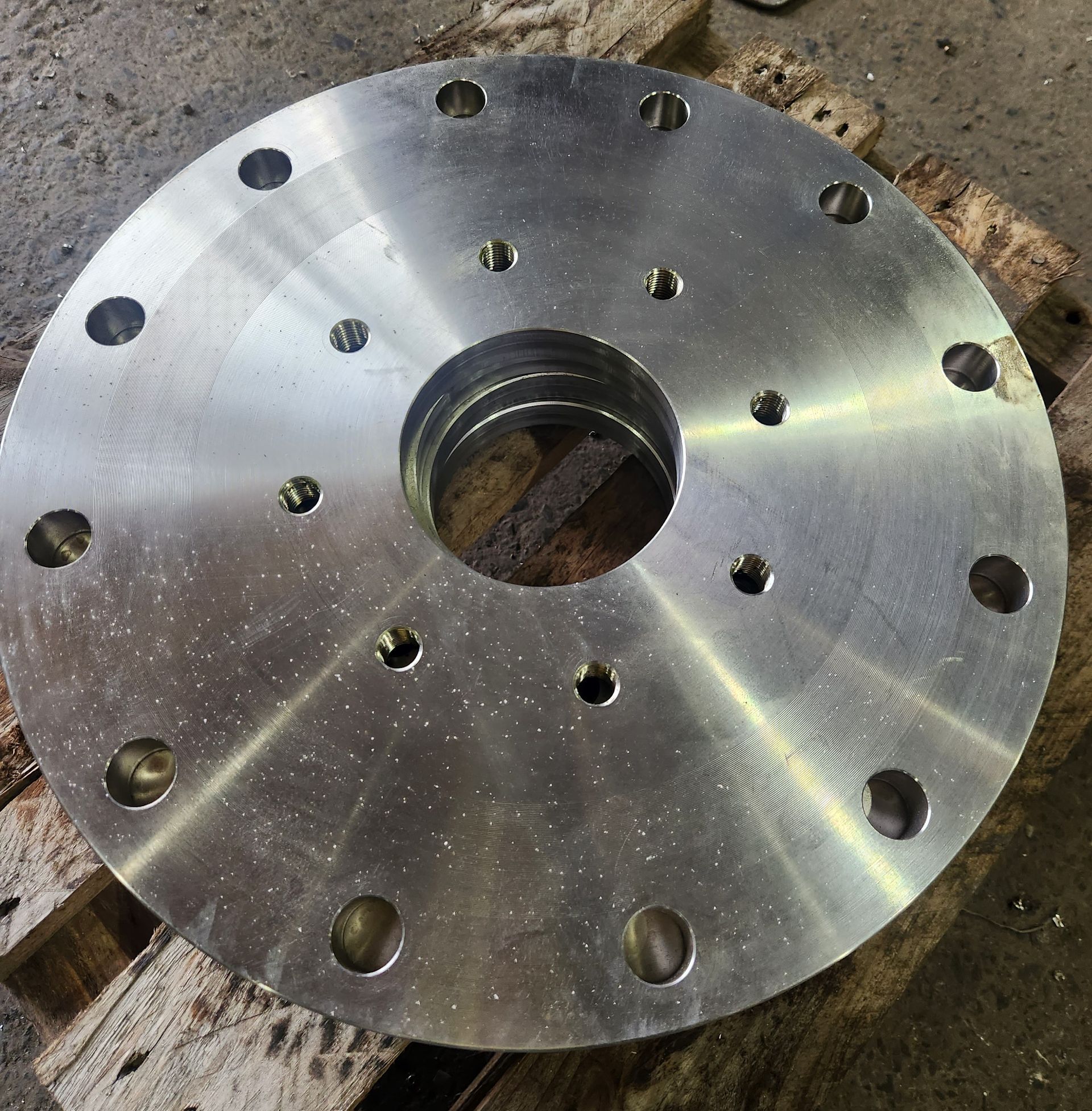 A metal disc with holes in it is sitting on a wooden pallet.