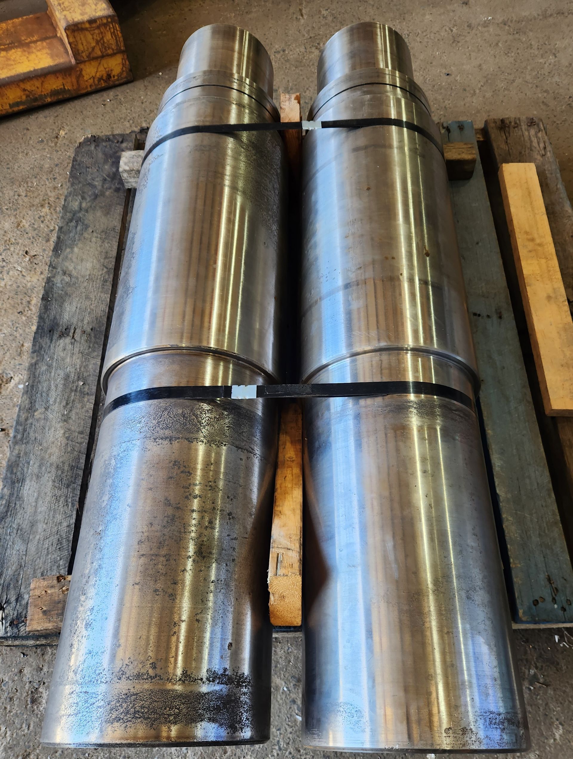 Two metal pipes are stacked on top of each other on a wooden pallet.