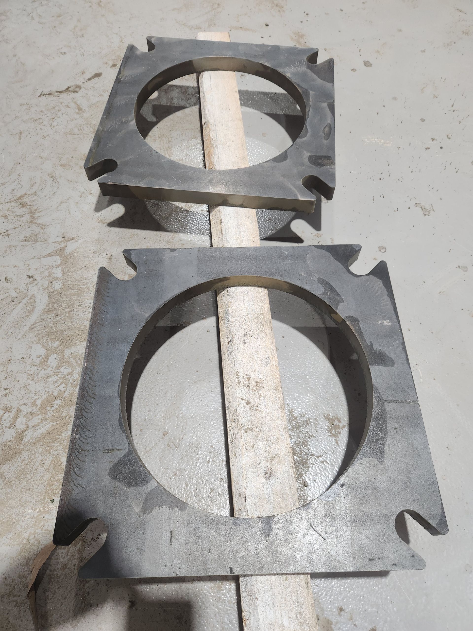 Two pieces of metal with holes in them are sitting on a wooden stick