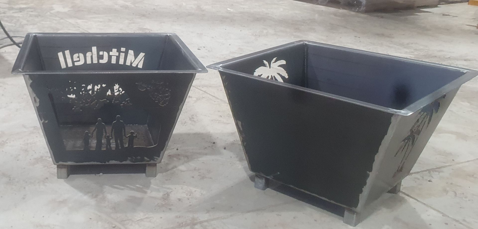 Two black planters are sitting next to each other on the ground.