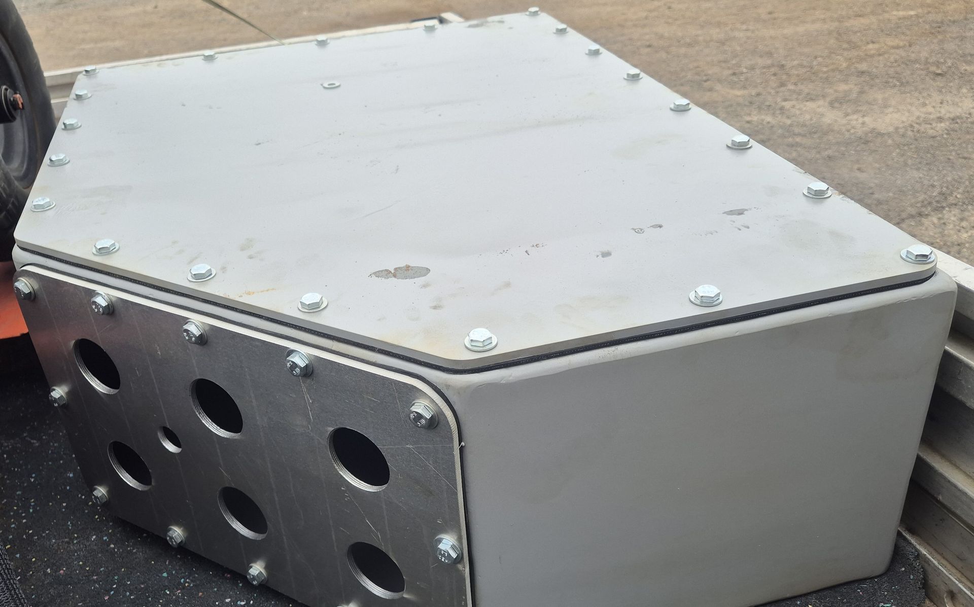 A metal box with holes in it is sitting on the ground