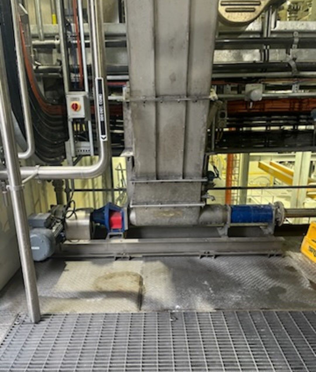 A stainless steel pipe is sitting on a metal floor in a factory.
