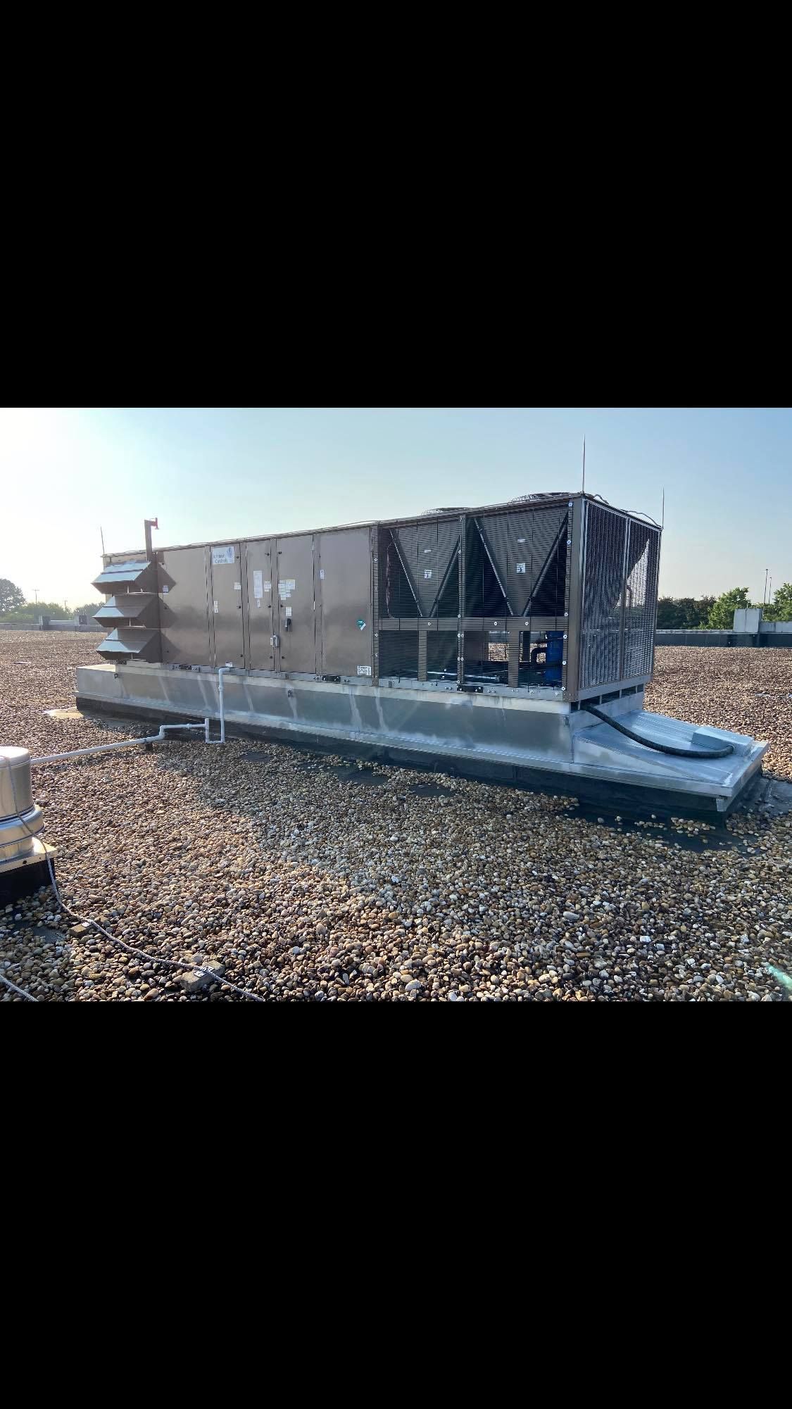 A large air conditioner is sitting on top of a gravel covered roof.