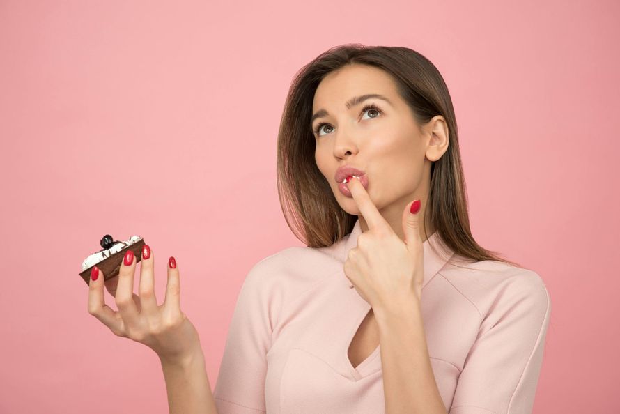 A woman is holding a cupcake in her hand and putting her finger in her mouth.