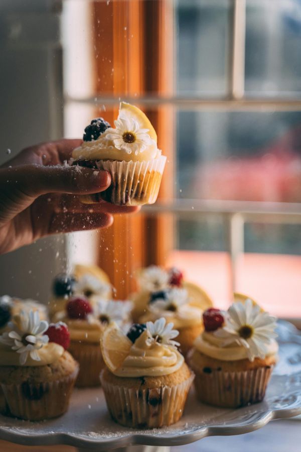 A person is holding a cupcake in their hand in front of a window.