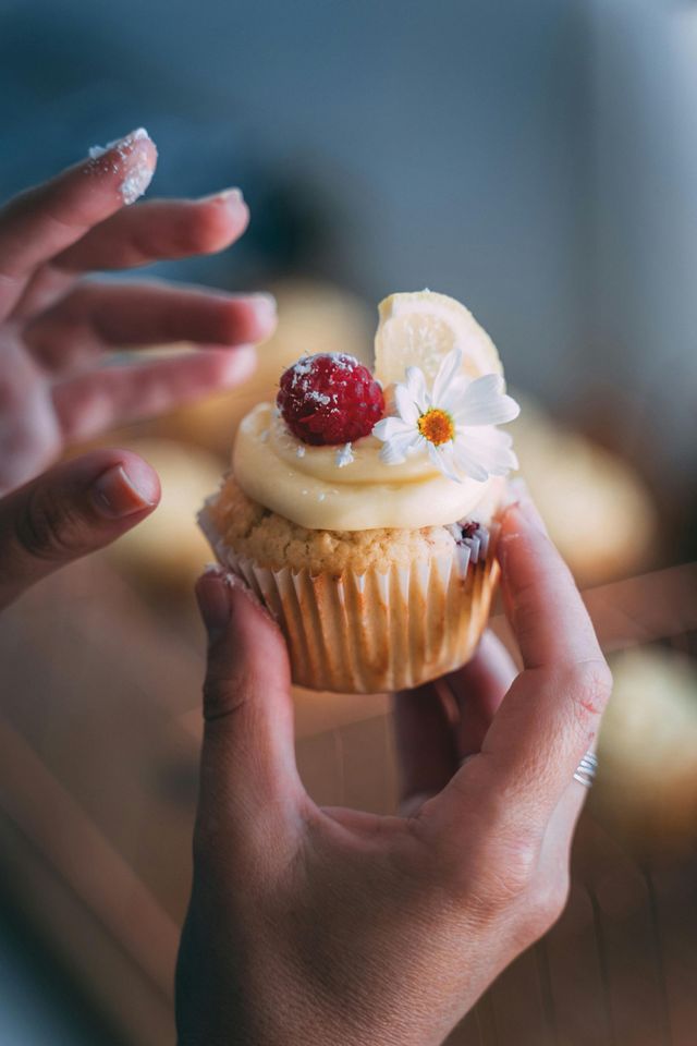 A person is holding a cupcake with a raspberry on top.