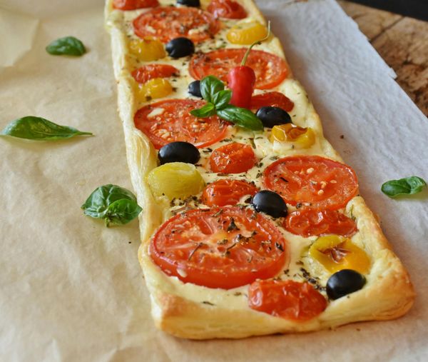 A long pizza with tomatoes and olives on it