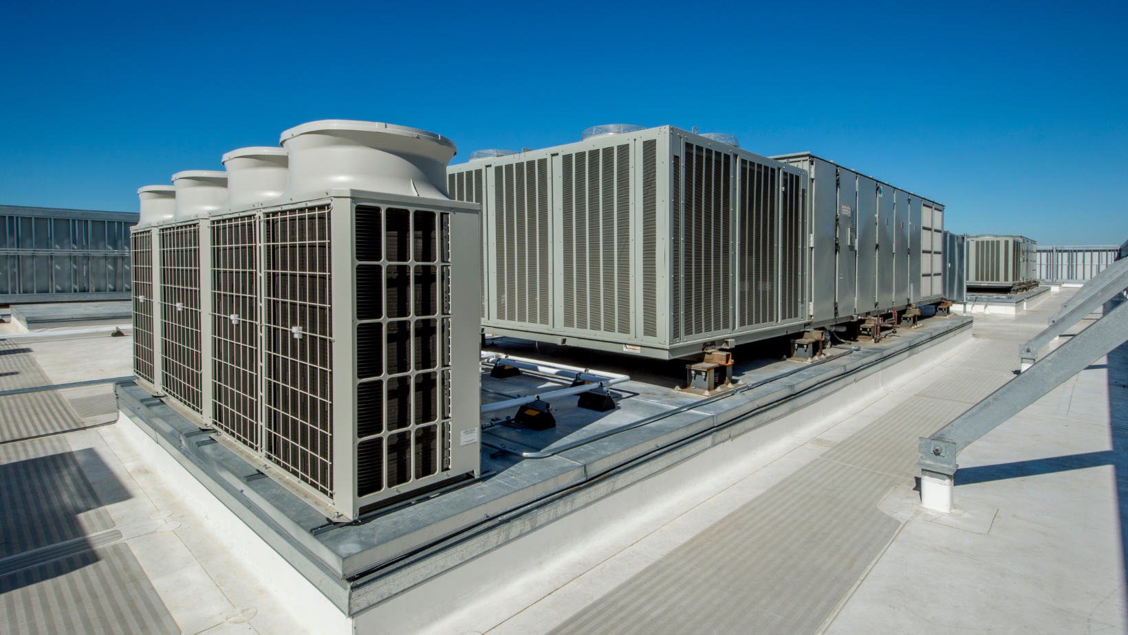 Rooftop HVAC units and large cooling towers on a flat industrial building under a clear blue sky