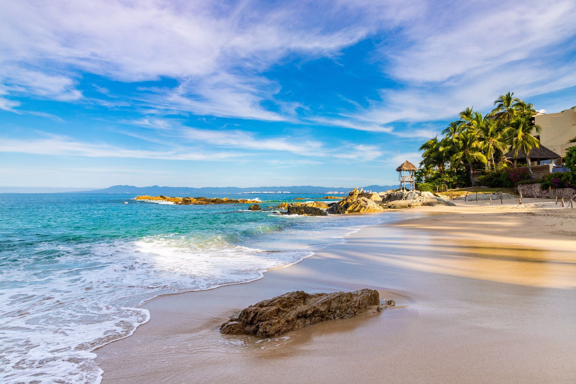 A beach with waves crashing on the sand and a house in the background. Vacation Travel Exclusives