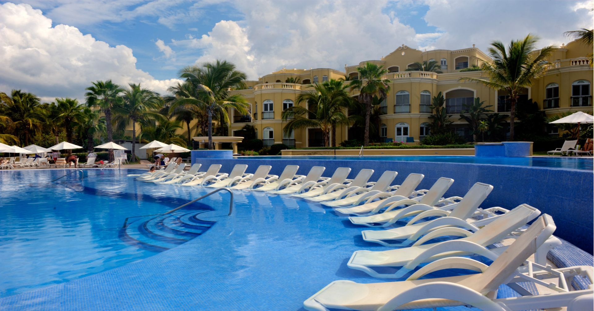 A large swimming pool surrounded by chairs and umbrellas. Vacation Travel Exclusives