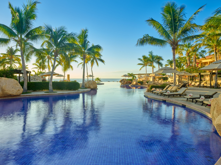 A large swimming pool surrounded by palm trees and chairs at a resort in Waikiki. Vacation Travel Exclusives
