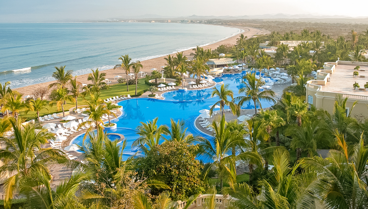 An aerial view of a large swimming pool surrounded by palm trees next to a beach in Waikiki. Vacation Travel Exclusives