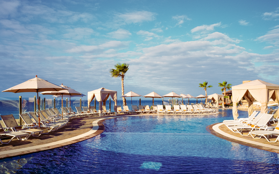 There is a large swimming pool with umbrellas and chairs around it. Vacation Travel Exclusives