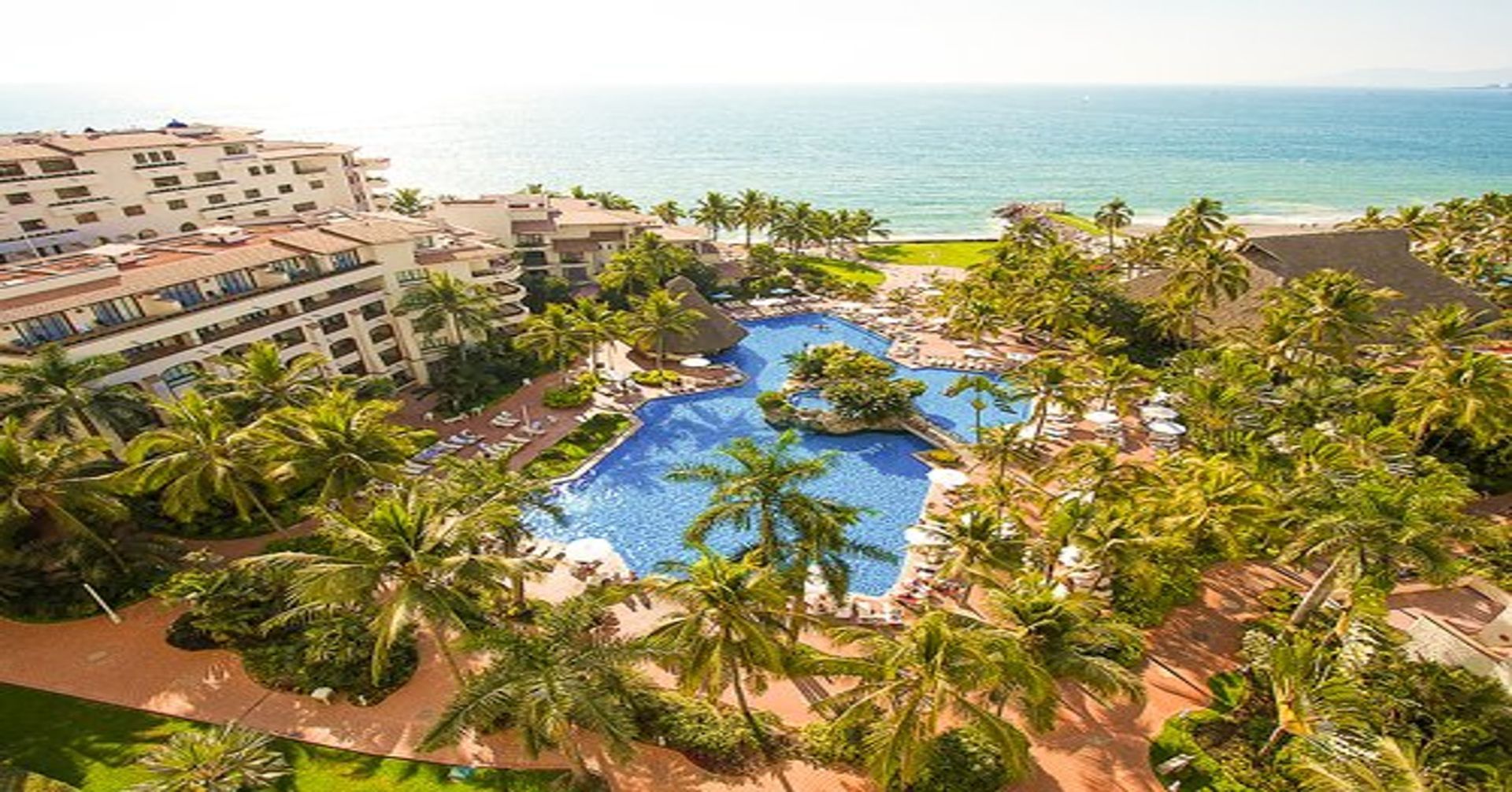 An aerial view of a resort with a large swimming pool surrounded by palm trees. Vacation Travel Exclusives