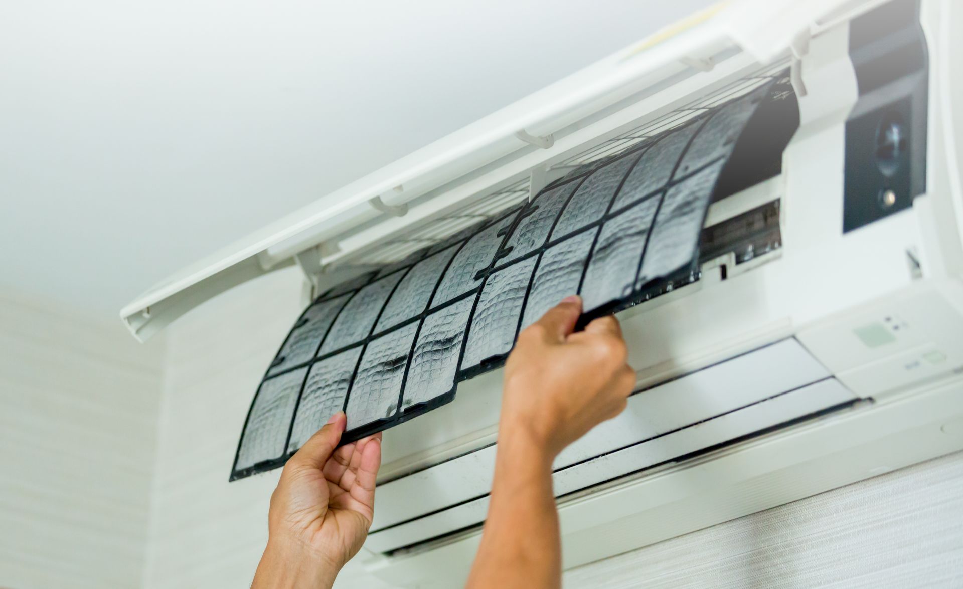 Person removing a dirty air filter from a white air conditioner unit.