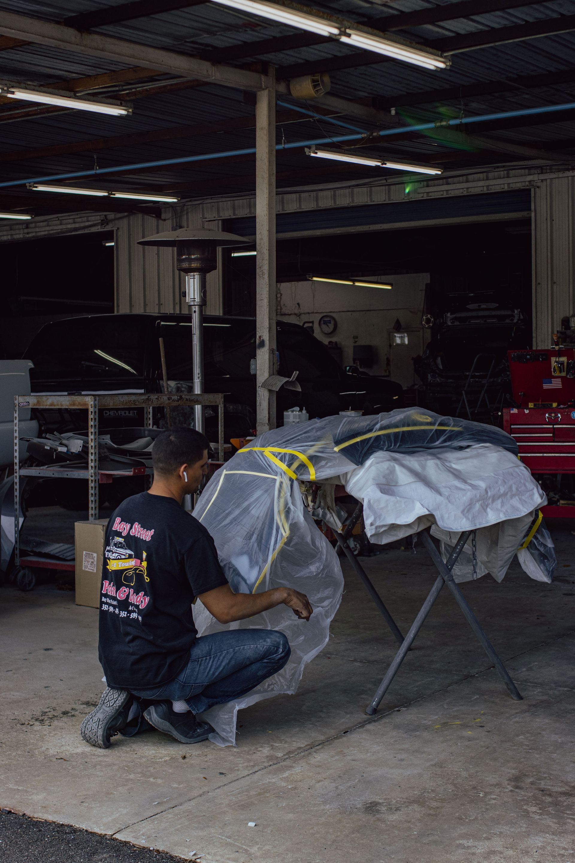 A man is working on a damaged red car with a hose - Eustis, FL - Bay Street Paint and Body