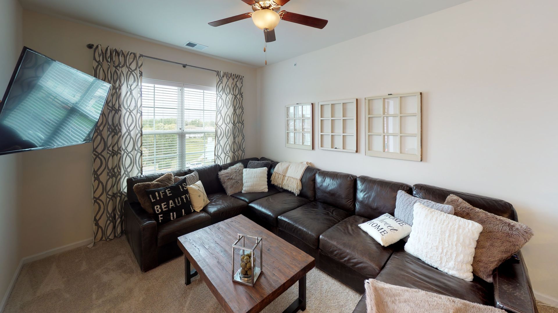 A living room with a couch , coffee table , television and ceiling fan.