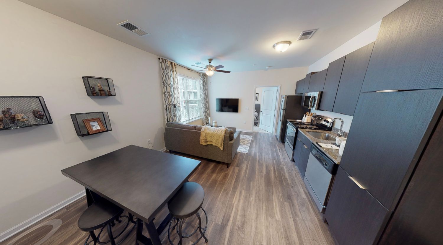 A living room with a table and stools and a kitchen.