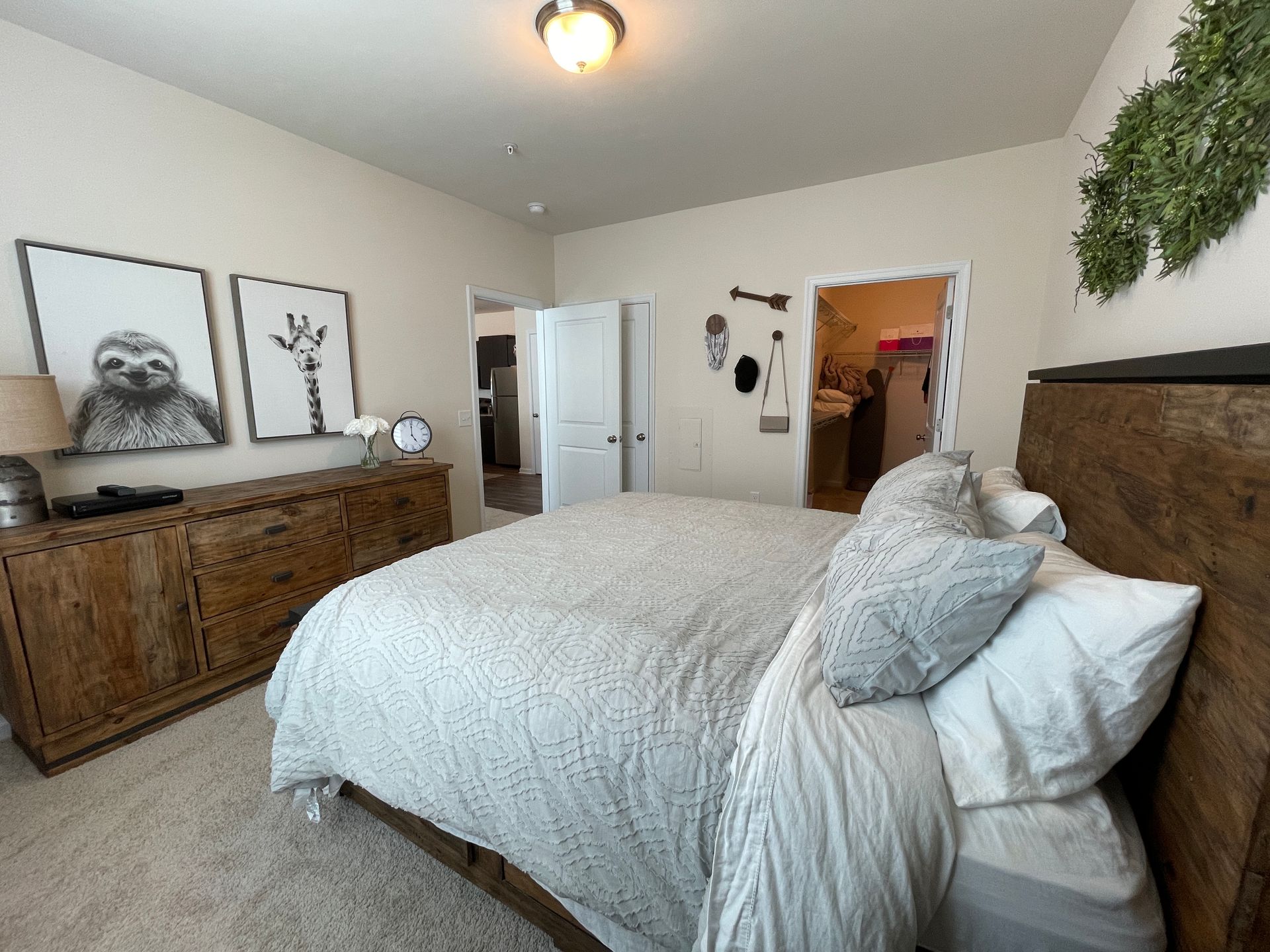 A bedroom with a bed , dresser , and paintings on the wall.