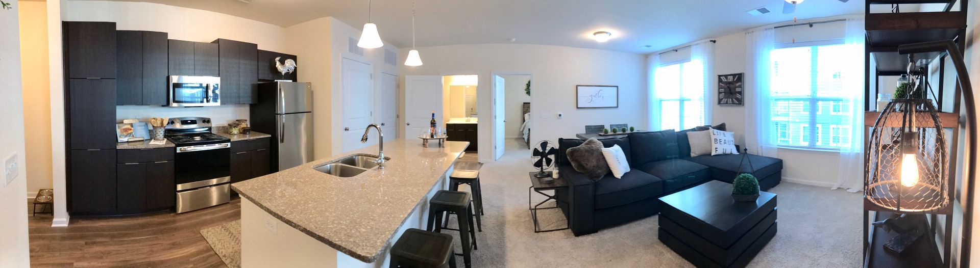 A panoramic view of a living room and kitchen in a house.