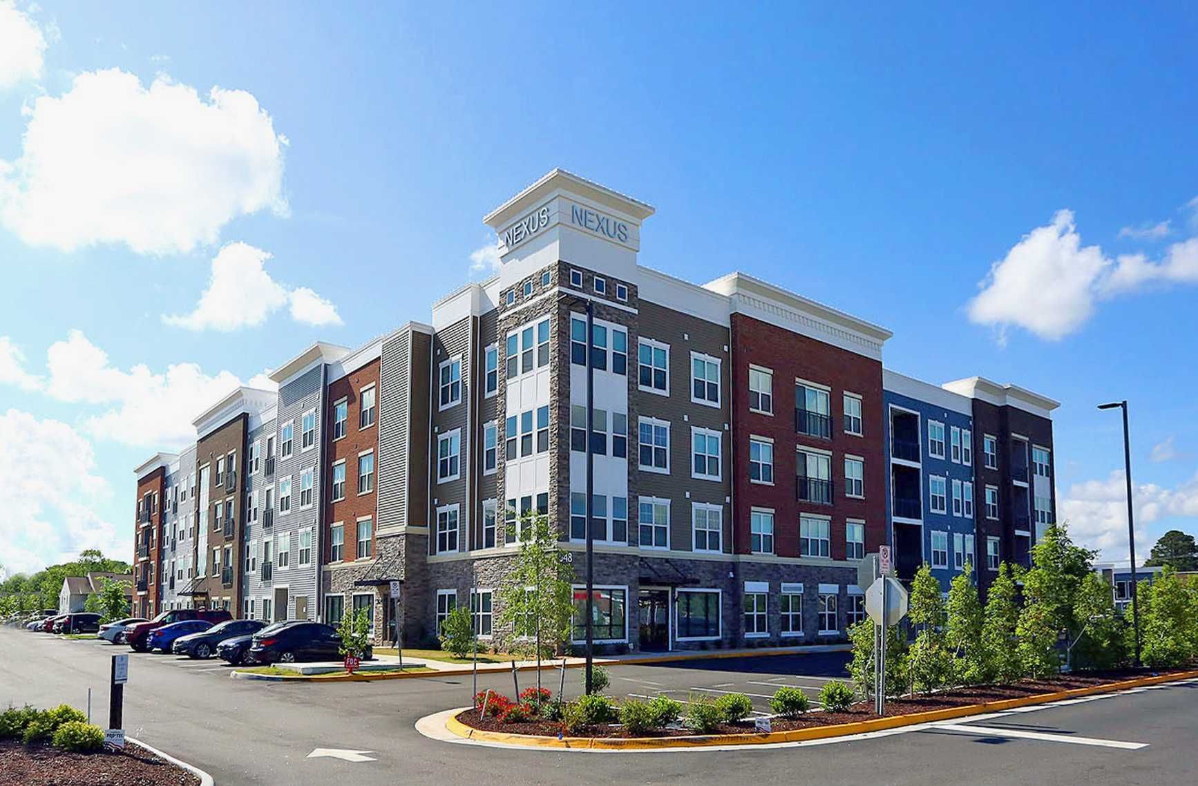 A large apartment building with cars parked in front of it on a sunny day.