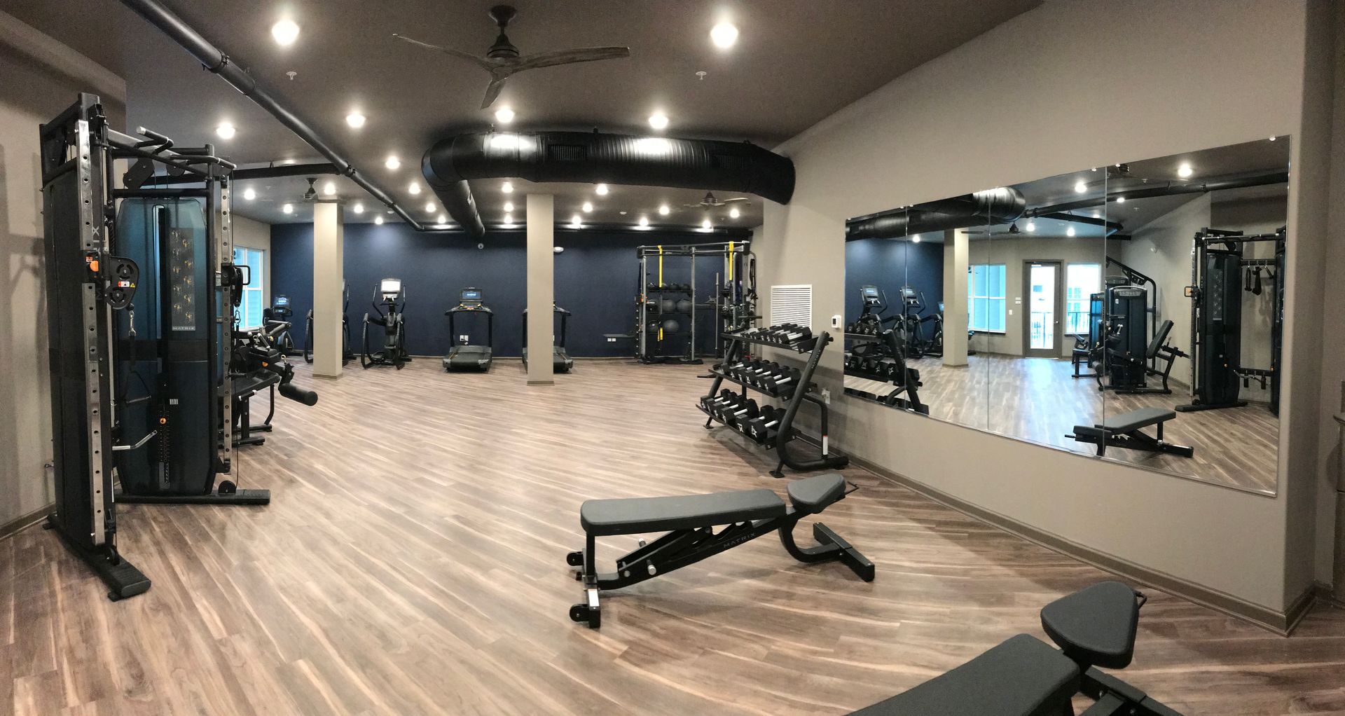 A large gym with a lot of equipment and a large mirror.