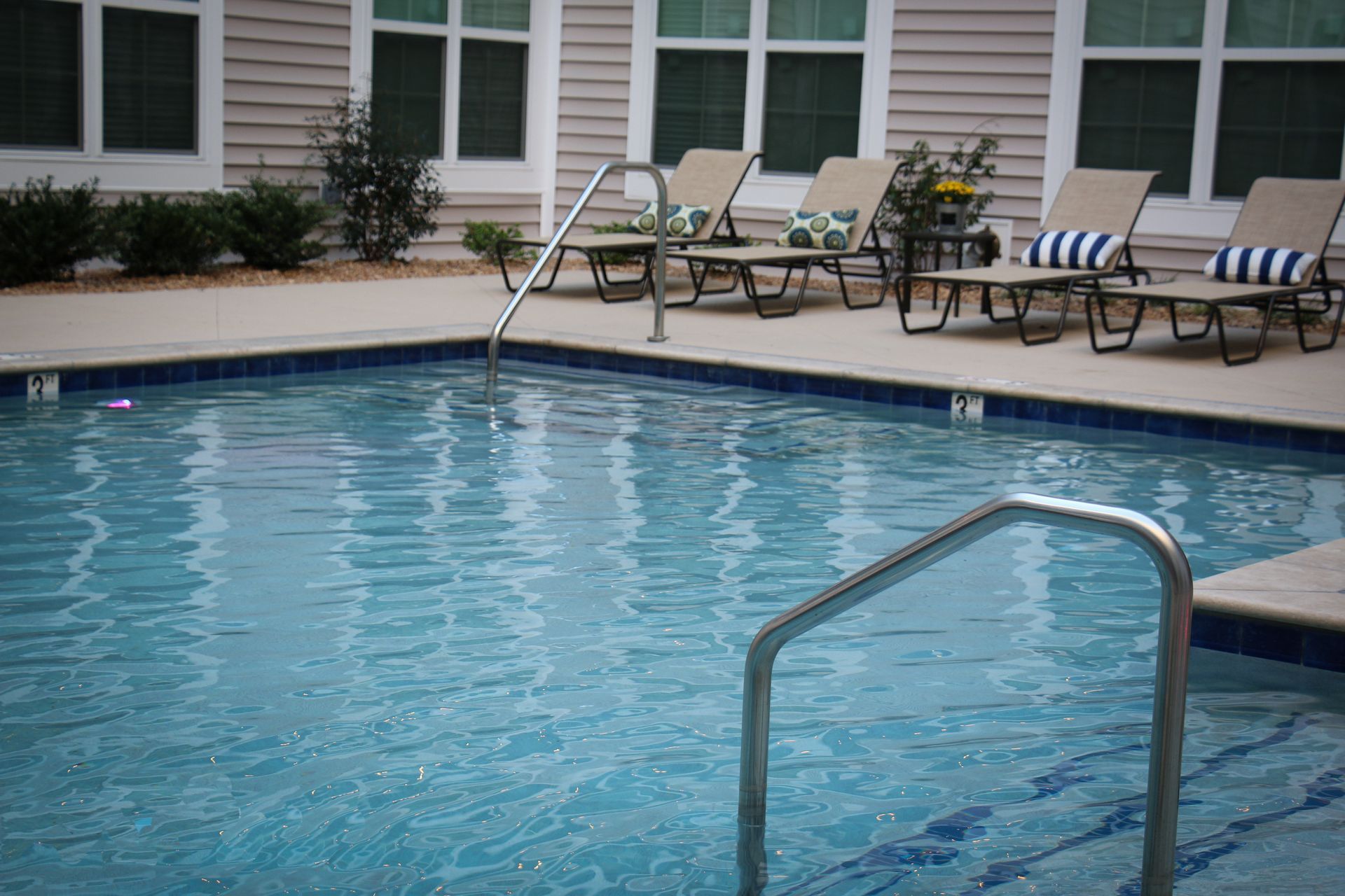 A large swimming pool surrounded by lounge chairs in front of a building.