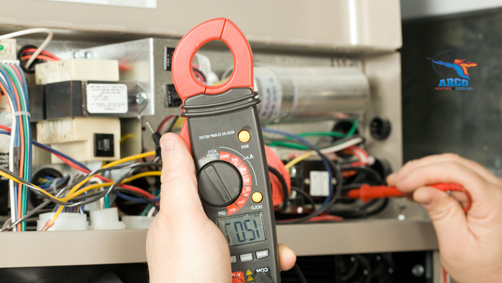 A person is holding a clamp meter in front of a furnace.