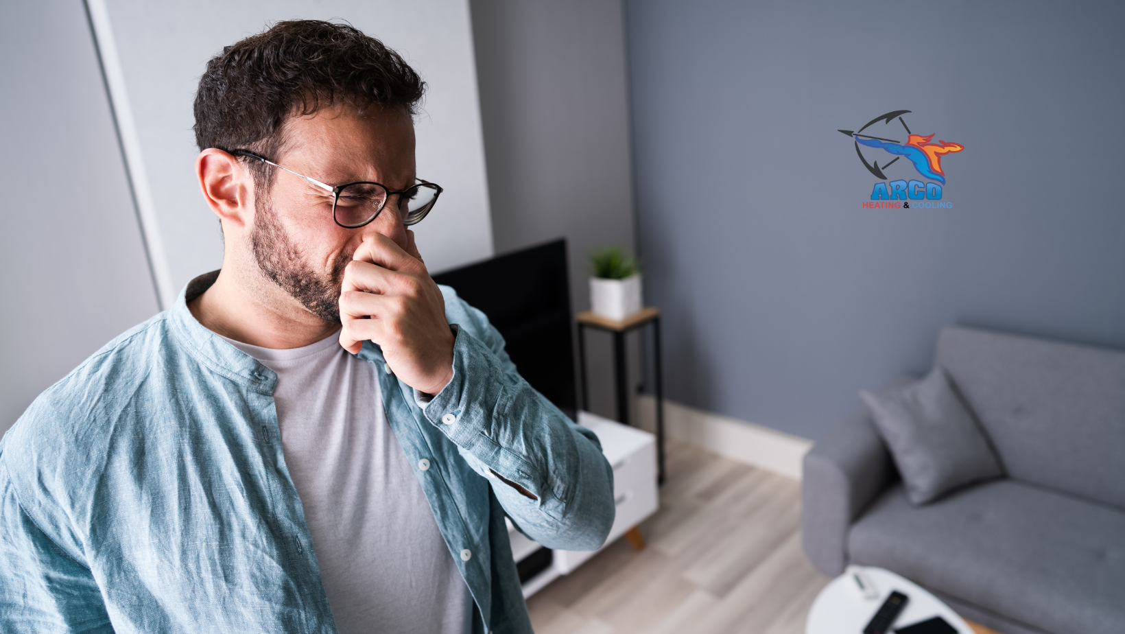 A man with glasses is covering his nose in a living room. A bad smell.