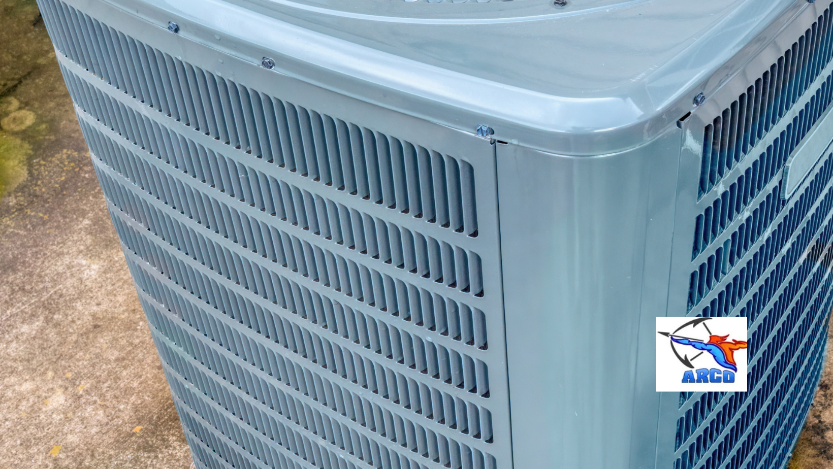 Gray outdoor air conditioning unit with vented sides, shown close up on a concrete surface.