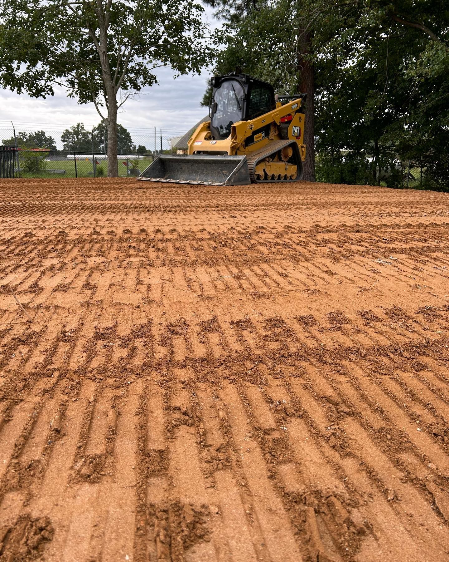 A small skid steer tractor smoothing red dirt, preparing a site for construction.