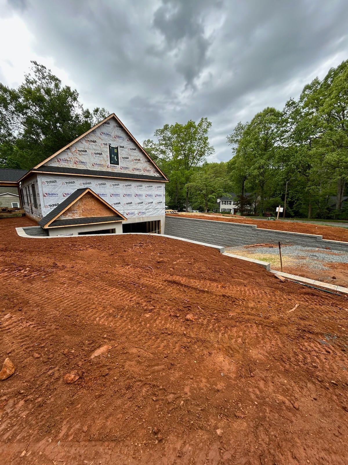 New house under construction with exposed framing and red dirt lot. Overcast sky.