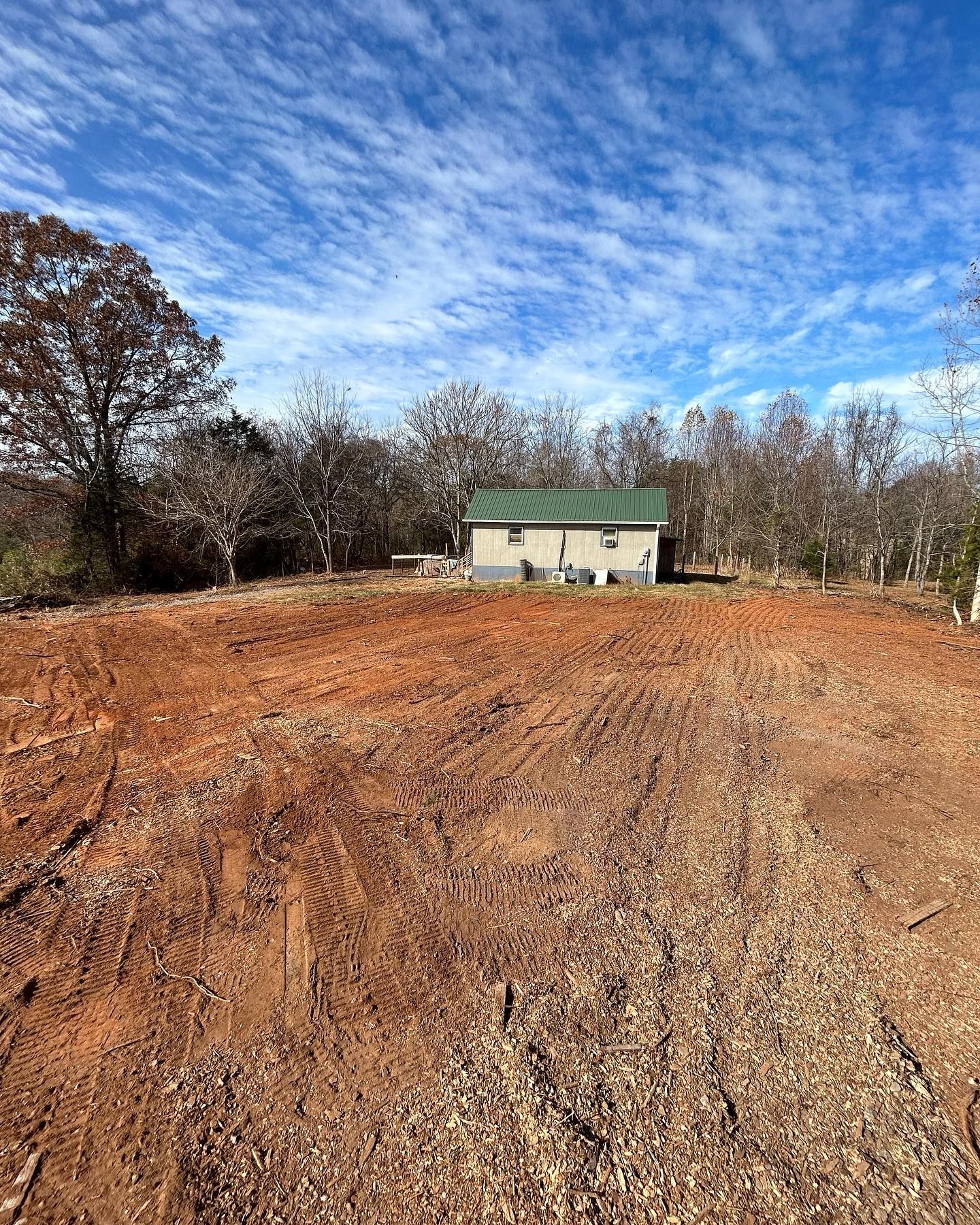 Cleared red dirt field with small building under a partly cloudy blue sky.