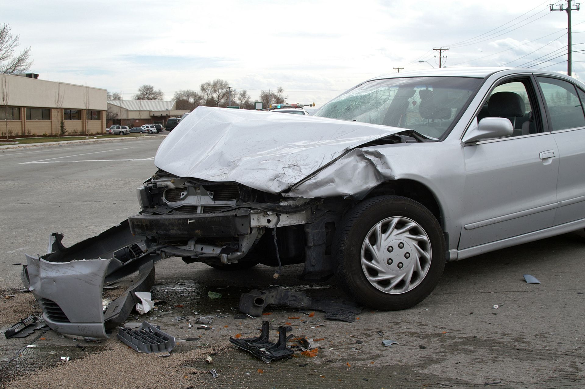 Silver car, extensively damaged in a front-end collision, debris on the ground.