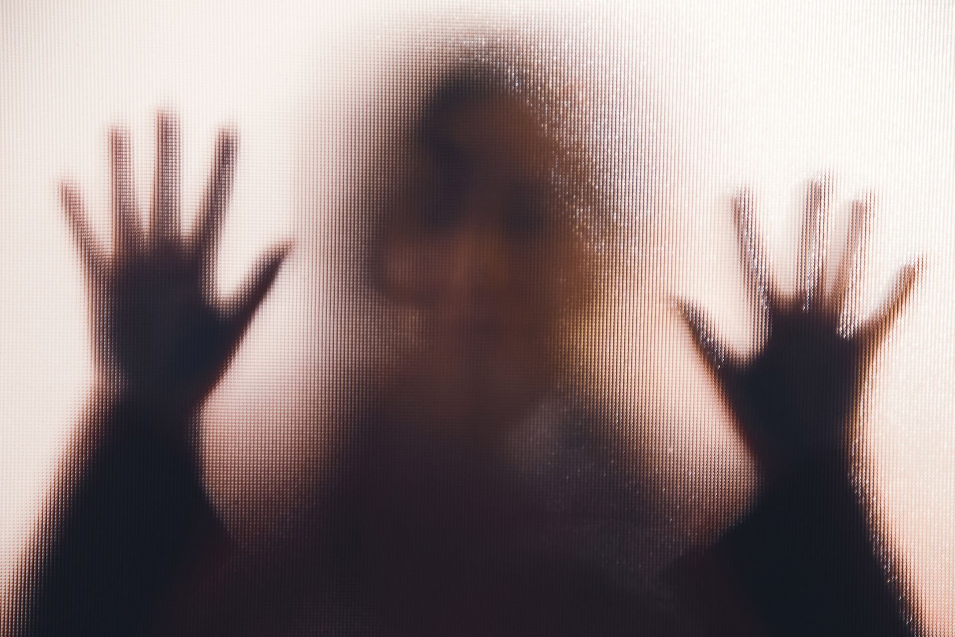 Silhouette of a person pressing hands against a textured, translucent surface.