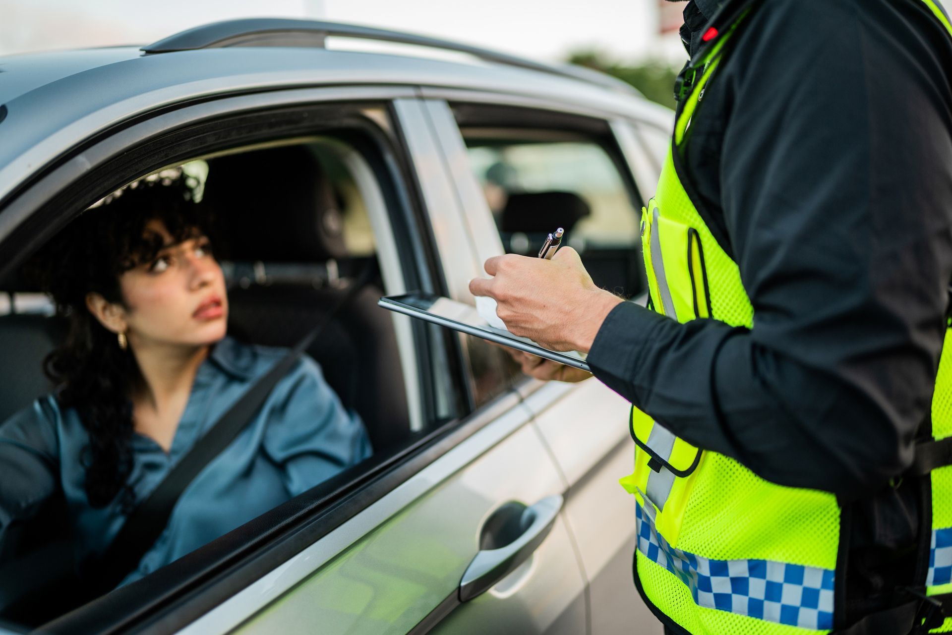 Woman in car looks at a police officer writing on a notepad. Officer is in high-vis vest.