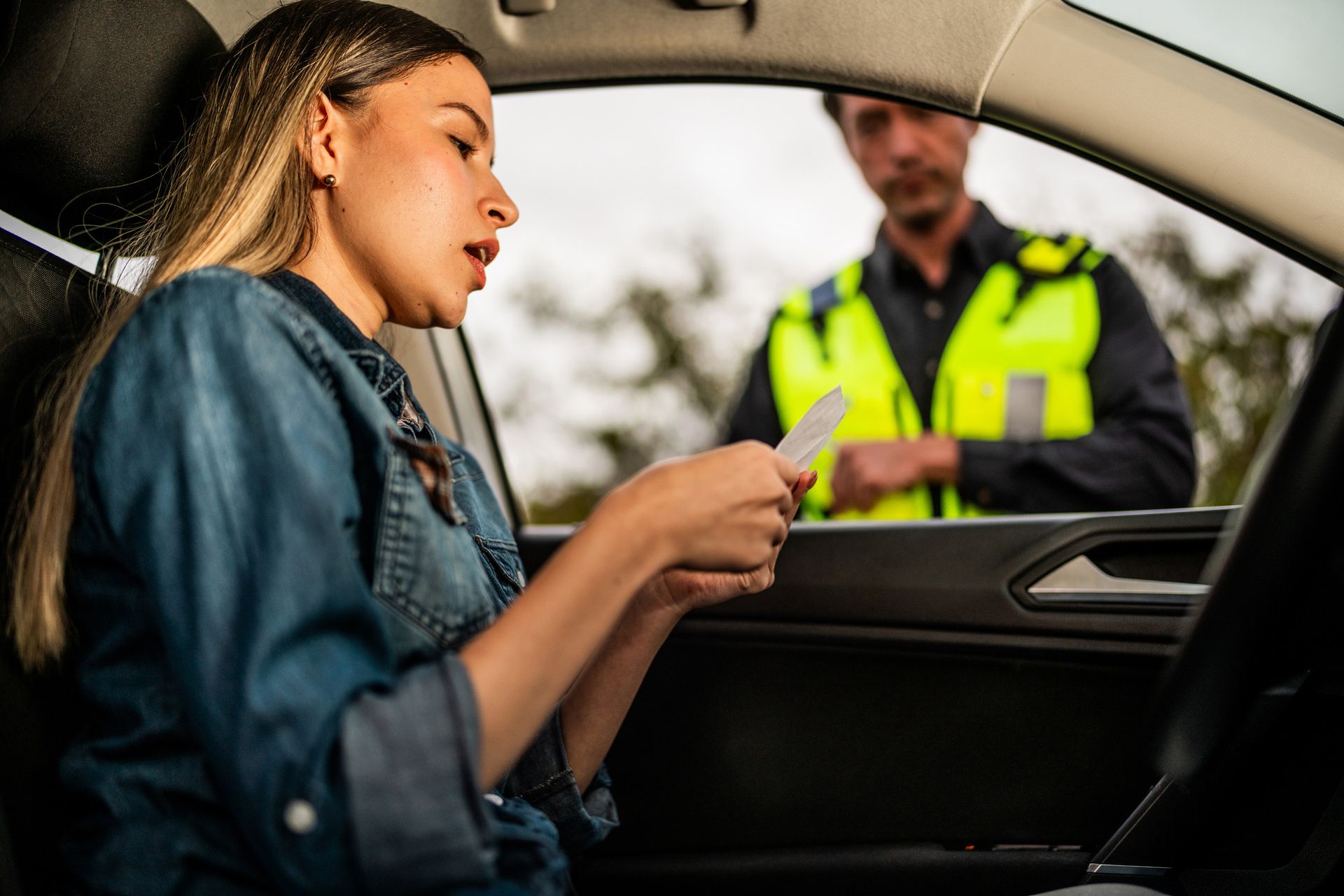 Woman in car showing driver's license to a police officer in a reflective vest.