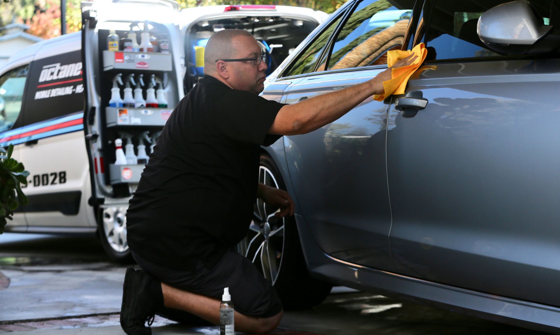 A man is kneeling down and cleaning a car with a towel.
