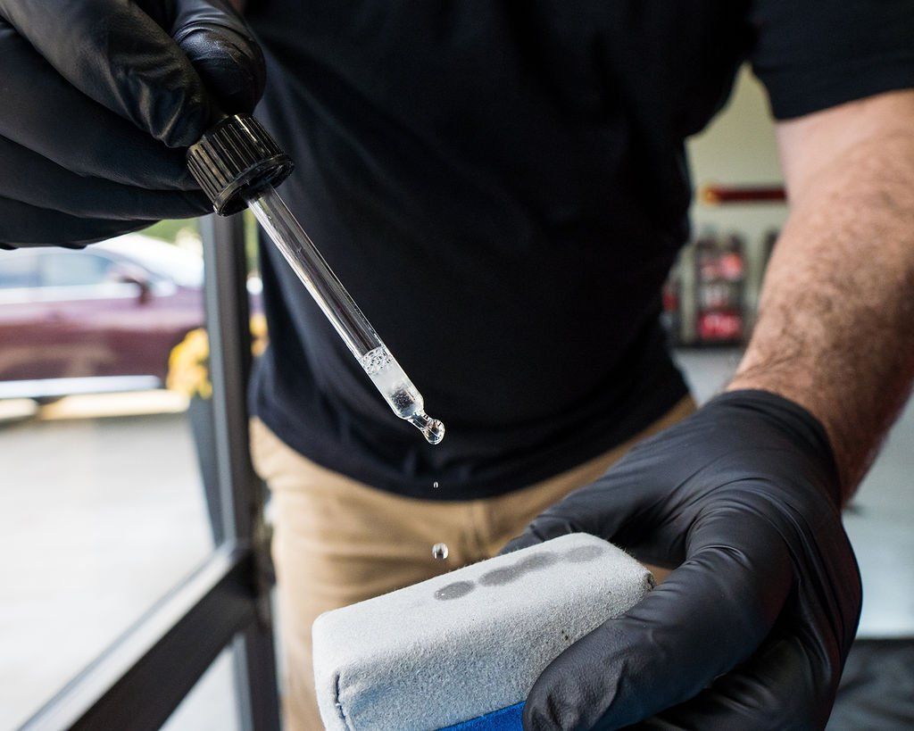 Person in black gloves using a dropper to apply liquid onto a gray applicator sponge.
